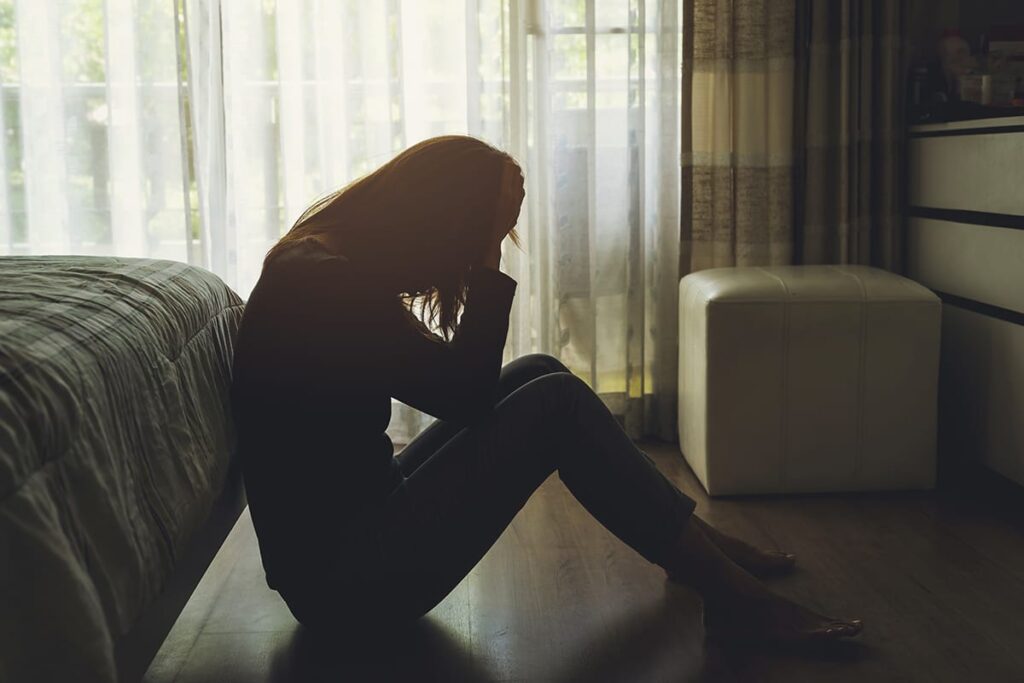 a person struggling with blackout drinking sits on a floor with their head in their hands